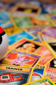 A Poké Ball resting among scattered vintage trading cards, representing the transformation of childhood hobbies into valuable collectibles