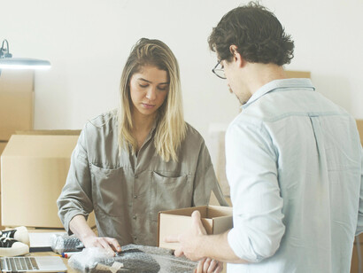 A man and a woman are wrapping products at a table in a small business warehouse