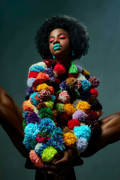 A foto apresente uma mulher com uma roupa singular e vibrante. A expressão da modelo traduz o poder da moda como linguagem e instrumento de transformação