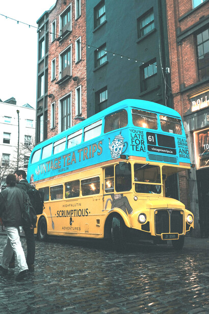 A blue and yellow vintage double-decker bus on a rain-soaked cobblestone street in Dublin, Ireland