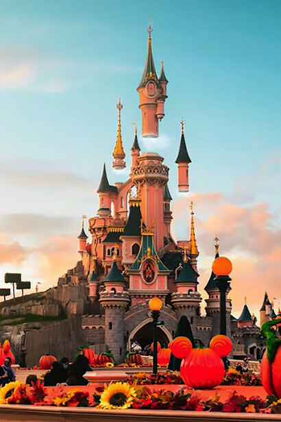 Daytime visitors pass by a brown concrete building on the sidewalk at Disneyland Paris in Marne-la-Vallée, France