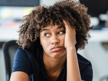 Portrait of a woman at a desk resting her face on her hand, appearing tired and lost in deep thought