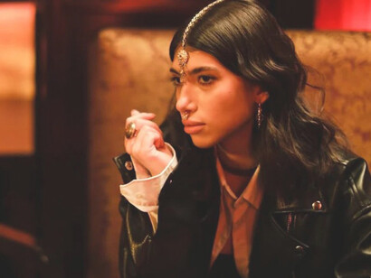 "An Indian woman wearing a leather jacket, adorned with a maang tikka and septum piercing, gazes into the distance