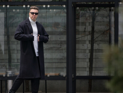 A stylish man in a black overcoat and sneakers captured in an urban setting