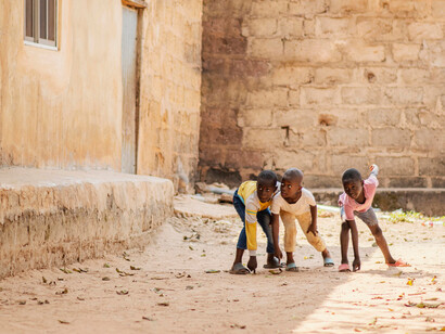 Quatre enfants s’apprêtent à courir dans une rue poussiéreuse, illustrant l’innocence de l’enfance même dans des environnements modestes