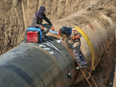 A man in a black jacket and blue denim jeans is sitting on a pipeline, making repairs during the day in Turkey