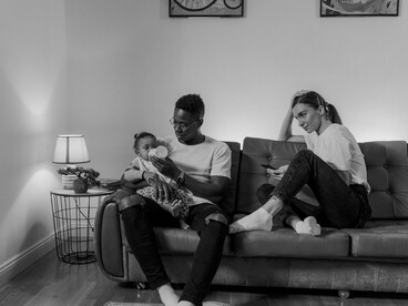 Pais dividem a atenção entre a criança e o telefone celular durante um momento de cuidado familiar. O artigo questiona o afastamento do diálogo e da partilha que tradicionalmente uniam as famílias