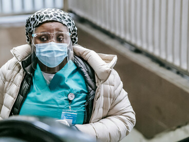 A Black nurse wearing a mask rides the escalator in the underground, unnoticed by the people around her
