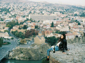 A young woman sitting on a hill above the city, gazing out over the urban landscape in solitude
