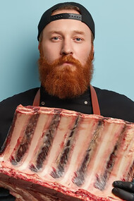 A man with a ginger beard, wearing an apron and gloves, holding high-tech food meat