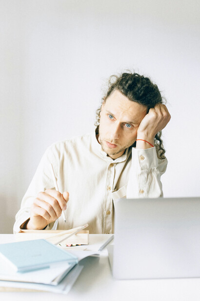 Exhausted young man sitting at a cluttered desk under work pressure, reflecting modern workplace stress, overthinking, and Gen-Z mental health struggles