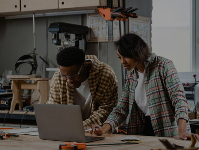 Man and woman using a laptop in a carpentry workshop, showcasing skilled teamwork and a creative workplace culture