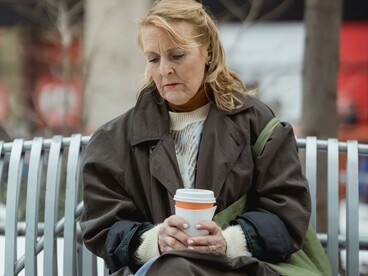 Melancholic woman sitting alone on a city bench, holding a takeaway coffee as the urban world moves around her