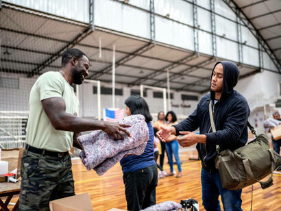 A young man being given a blanket by a volunteer in a shelter