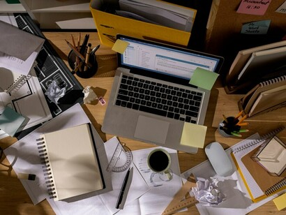 The cluttered office desk, combined with the fast-paced world and digital anxiety, creates a stressful and overwhelming environment