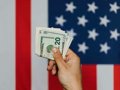 Person hält eine amerikanische Banknote vor einer US-Flagge hoch