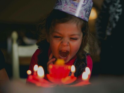 A toddler screaming at her birthday cake candles in an attempt to extinguish the flames