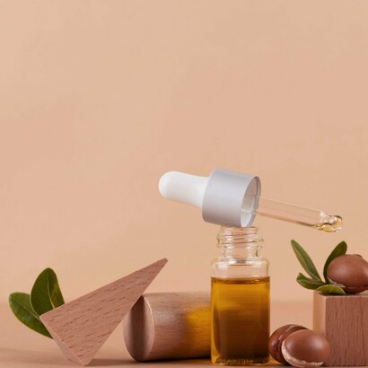 A bottle of argan oil with a dropper, surrounded by natural elements, suggests easy and precise application for moisturizing coily and textured hair