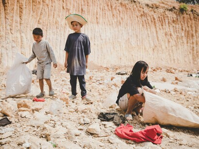Under the harsh sun, three children sift through the dust and debris, their small hands searching for anything of value, a stark reminder of the deep divide between privilege and poverty