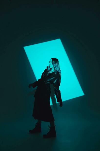 Modella in trench di pelle nero su set fotografico di sfondo verde acqua