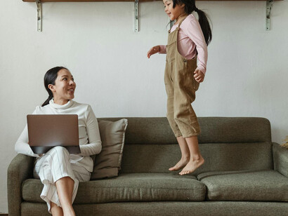 Mujer sentada en un sillón y niña saltando a su lado