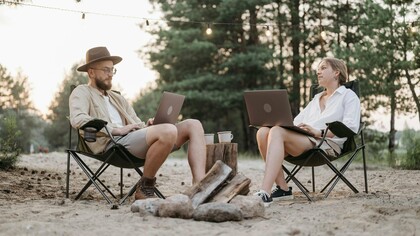 Sentados diante do verde, um casal trabalha em meio à natureza. Talvez a utilidade também precise respirar longe da produtividade constante. Há inutilidades necessárias que fazem a vida florescer