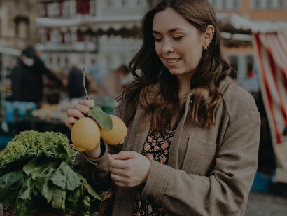 A woman food shopping at the farmer's market is contemplating purchasing a couple of lemons