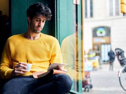 A man quietly records his thoughts in a diary while sitting by an autumn-lit window