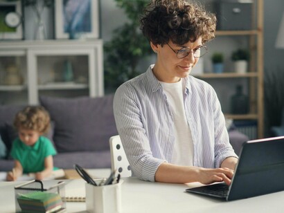 A mother focused on her work as her child plays quietly in the background, representing the delicate balance between career and parenting