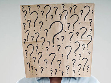 A person wearing a paper bag on their head, with question marks drawn on it