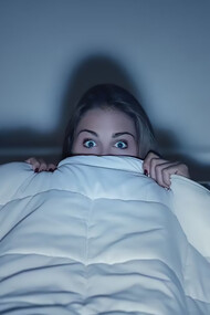 A woman, wrapped in a blanket, enjoying a horror movie with a frightened expression