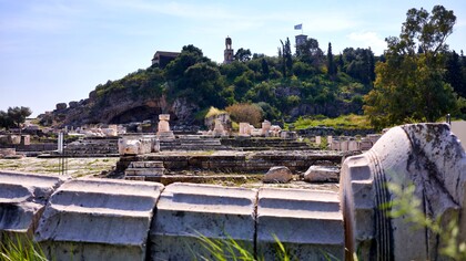 Sito archeologico del santuario di Demetra a Eleusi. Il cortile del santuario a sinistra, sopra la scalinata i Propilei Maggiori. Accanto alla caverna sullo sfondo si trovava il santuario di Plutone: la caverna rappresenta l'ingresso agli Inferi. Il sentiero a sinistra della caverna conduce al Telesterion, dove i fedeli venivano iniziati ai misteri eleusini. Eleusi, Grecia