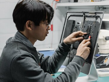 A technician carefully repairing an electronic device at a workbench, representing the importance of repairing and extending the lifespan of electronics to reduce e-waste