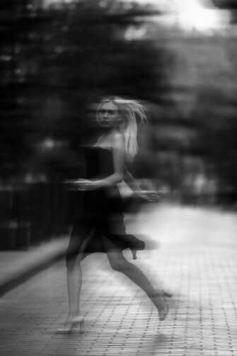 An artistic black and white image of a woman strolling down a blurred sidewalk
