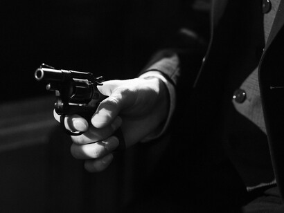 A man in a dark suit clutches a revolver, evoking the stylized aesthetic of noir crime films that influence true crime storytelling