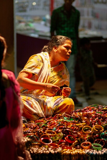 In Hyderabad, Telangana, India, a woman dressed in traditional attire adorned with bracelets sits gracefully at a vibrant bazaar