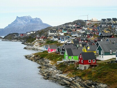Casas coloridas acompanham a costa e avançam pelas encostas rochosas de Nuuk, diante das montanhas que cercam a cidade. A ocupação urbana convive diretamente com a paisagem natural que caracteriza a Groenlândia
