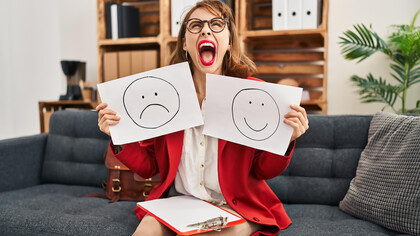 A young woman is holding papers with an unhappy face in one hand and a happy face in the other