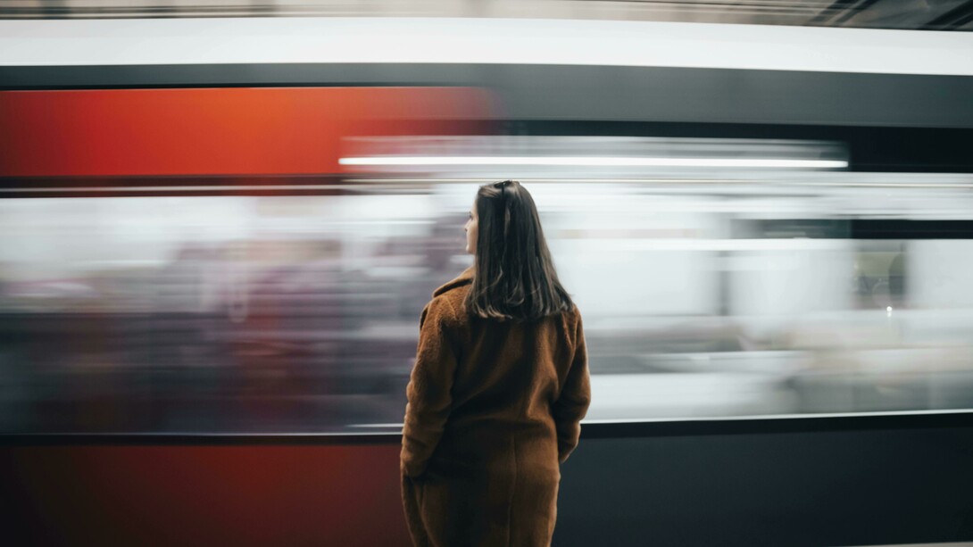 Woman in a brown coat standing alone as a speeding train passes by