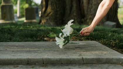 Un mujer deja unas flores encima de la tumba de un ser querido
