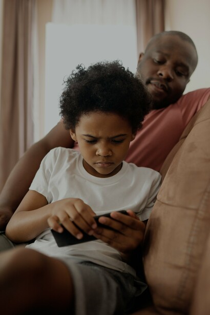 A father looking at his child, who is playing on a phone
