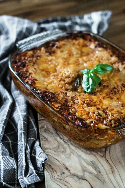 A delicious plate of lasagna served on a wooden table, with a glass of wine beside it
