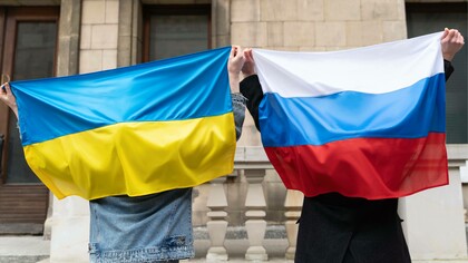 Due mani che reggono due bandiere che non si guardano mai davvero. L’azzurro e il giallo dell’Ucraina tremano nell’aria come un respiro trattenuto; il bianco, il blu e il rosso della Russia pesano come una memoria che non trova pace. Tra i due c’è uno spazio invisibile, carico di storia, di dolore e di parole non dette. Le bandiere sono ferite aperte e identità che si cercano e si respingono. Eppure, nelle mani che le sorreggono, resta un gesto umano, fragile e potente