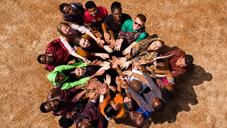 People from diverse backgrounds gather in a circle in Masimba, Tanzania, expressing solidarity and community through a shared gesture of unity