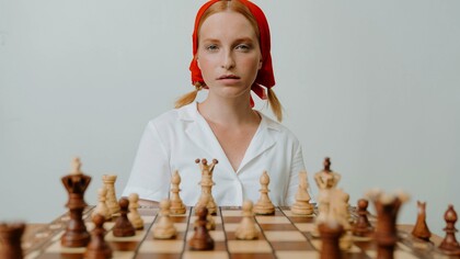 Mulher de camisa branca joga xadrez no tabuleiro de madeira marrom