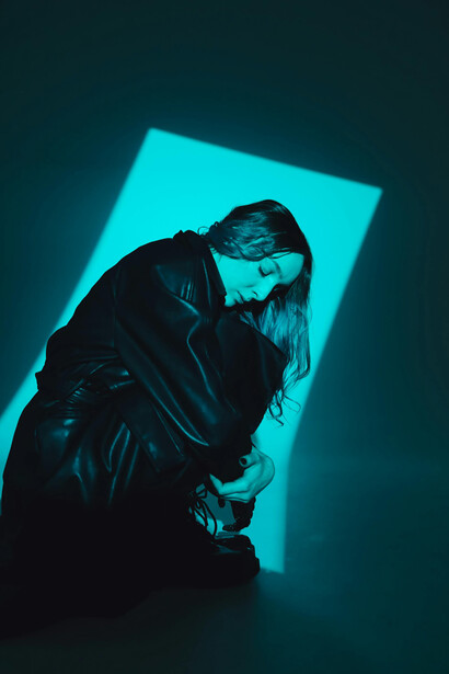 Modella in trench di pelle nero su set fotografico di sfondo verde acqua