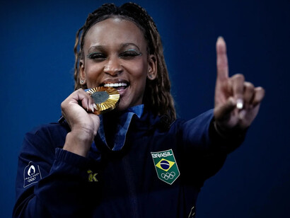 Rebeca Andrade morde medalha de ouro conquistada pelo solo nos Jogos Olímpicos de Paris 2024. Foto: Alexandre Loureiro/Comitê Olímpico Brasileiro