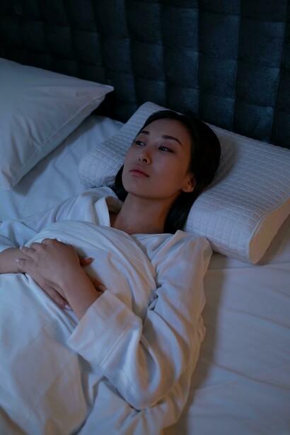 A woman in white sleepwear sits on a bed, struggling with insomni