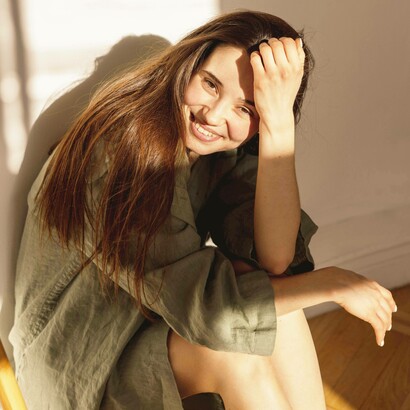 Giovane donna sorridente in una stanza e illuminata dalla luce del sole: "Proviamo ad essere semplicemente umani"