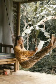 A woman sitting on a hammock, holding a sketchbook during a quiet afternoon